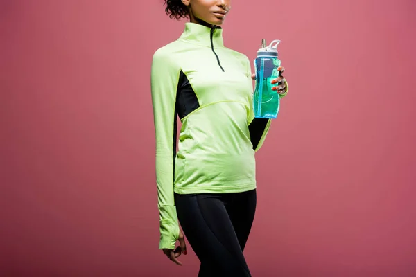 Partial view of african american sportswoman in track jacket with sport bottle isolated on brown — Stock Photo