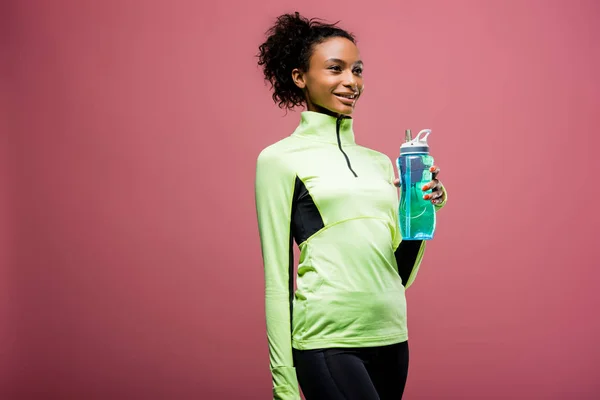 Hermosa deportista afroamericana en chaqueta de atletismo con botella de deporte aislado en marrón con espacio de copia - foto de stock