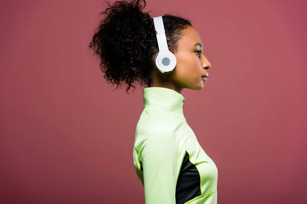 Vue latérale de belle sportive afro-américaine dans des écouteurs isolés sur brun — Photo de stock
