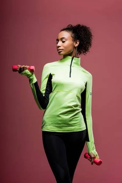 Beautiful african american sportswoman training with dumbbells isolated on brown — Stock Photo