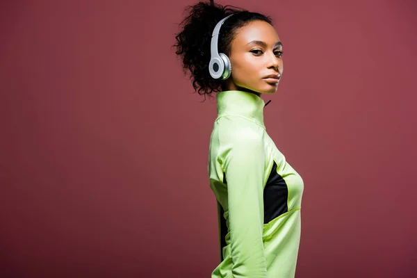 Beautiful african american sportswoman in headphones looking at camera isolated on brown with copy space — Stock Photo