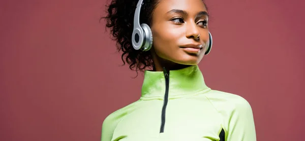 Panoramic shot of beautiful african american sportswoman in headphones isolated on brown with copy space — Stock Photo