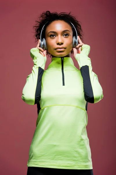 Красивая африканская американская спортсменка в наушниках и спортивной куртке, изолированной на коричневом — стоковое фото