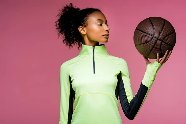 Bela esportista afro-americana com basquete isolado em rosa — Fotografia de Stock