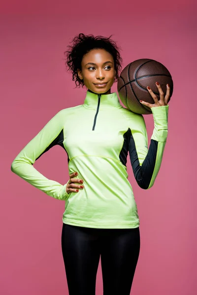 Belle sportive afro-américaine avec la main sur la hanche tenant basket isolé sur rose — Photo de stock