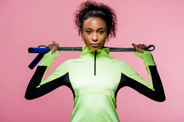 Красивая африканская американская спортсменка смотрит в камеру, позируя с скакалкой, изолированной на розовом — стоковое фото