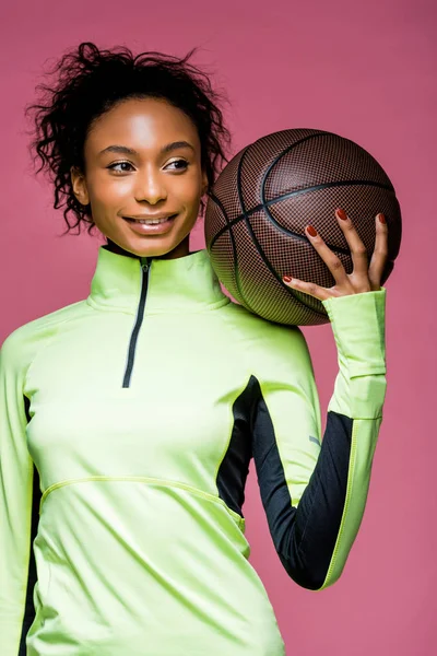 Schöne lächelnde afrikanisch-amerikanische Sportlerin hält Basketball isoliert auf rosa — Stockfoto