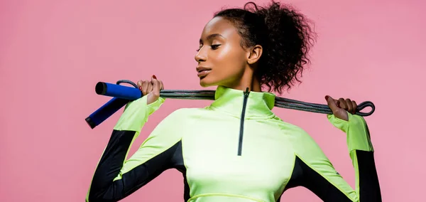 Plano panorámico de la hermosa deportista afroamericana posando con la cuerda de saltar aislado en rosa - foto de stock