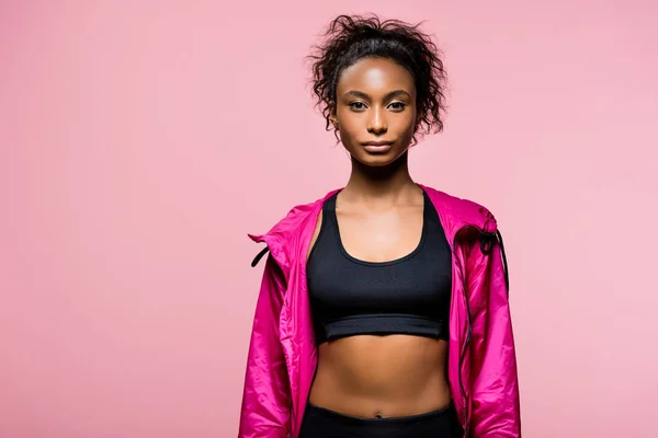 Selbstbewusste attraktive afrikanisch-amerikanische Sportlerin in Windjacke schaut in die Kamera isoliert auf rosa mit Kopierraum — Stockfoto