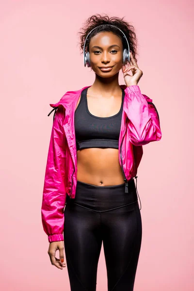 Schöne afrikanisch-amerikanische Sportlerin mit Kopfhörer, die in die Kamera schaut isoliert auf rosa — Stockfoto