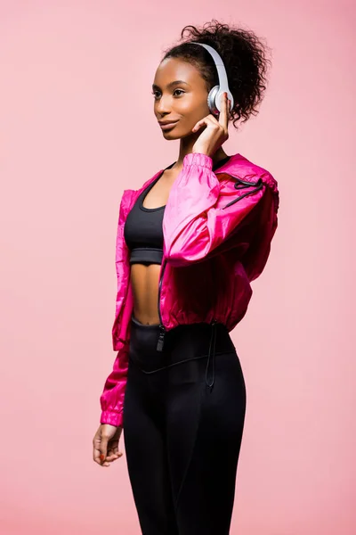 Schöne afrikanisch-amerikanische Sportlerin mit Kopfhörern, die isoliert auf rosa schaut — Stockfoto