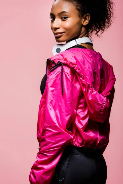 Hermosa afroamericana deportista con auriculares mirando a la cámara aislada en rosa - foto de stock