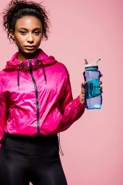 Belle sportive afro-américaine avec bouteille de sport regardant la caméra isolée sur rose — Photo de stock