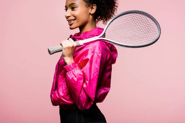 Красива усміхнена афроамериканська спортсменка тримає тенісну ракетку ізольовано на рожевому — стокове фото