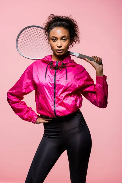 Beautiful african american sportswoman holding tennis racket and looking at camera isolated on pink — Stock Photo
