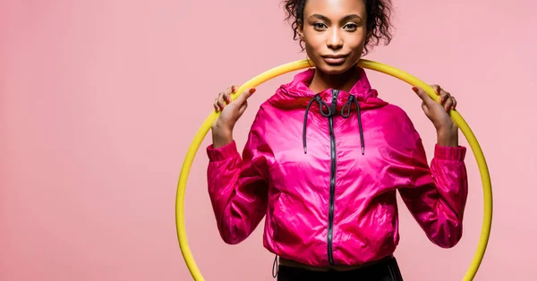 Colpo panoramico di bella sportiva afro-americana con hula hoop guardando la fotocamera isolata su rosa — Foto stock