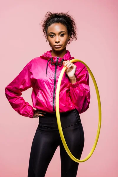Schöne afrikanisch-amerikanische Sportlerin blickt in die Kamera und hält Hula-Hoop-Reifen isoliert auf rosa — Stockfoto