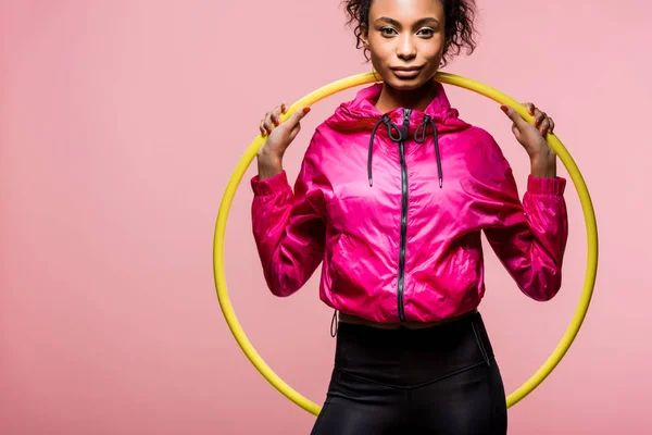 Schöne afrikanisch-amerikanische Sportlerin blickt in die Kamera und hält Hula-Hoop-Reifen isoliert auf rosa mit Kopierraum — Stockfoto