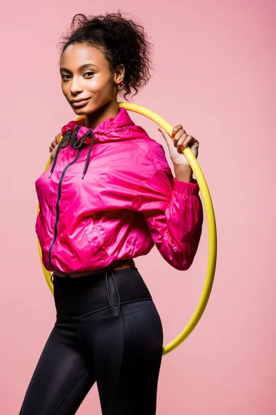 Красивая улыбающаяся африканская спортсменка, позирующая с обручем хула, изолированным на розовом — стоковое фото