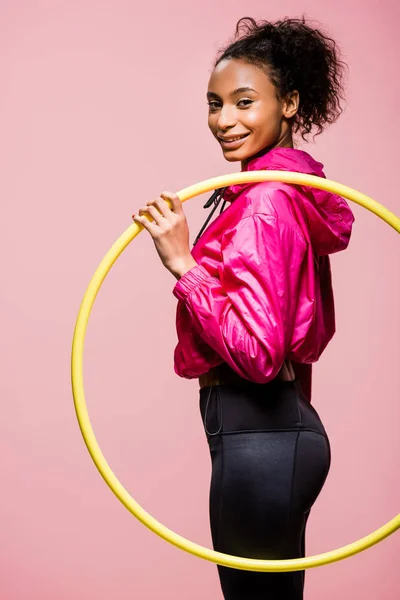 Красива усміхнена афроамериканська спортсменка позує з обручем ізольована на рожевому — стокове фото