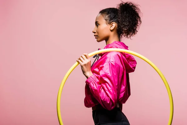 Side view of beautiful african american sportswoman posing with hula hoop isolated on pink with copy space — Stock Photo