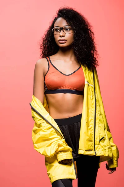 Beautiful african american sportswoman in glasses looking away and posing isolated on coral — Stock Photo