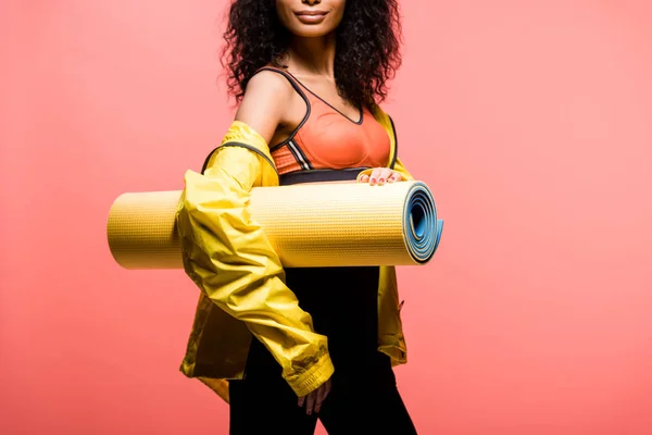Cropped view of african american sportswoman holding sport mat isolated on coral — Stock Photo