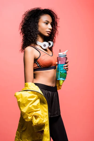 Belle sportive afro-américaine posant avec écouteurs et bouteille de sport isolée sur corail — Photo de stock