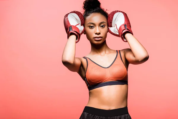 Bela esportista afro-americana em luvas de boxe olhando para a câmera isolada em coral — Fotografia de Stock