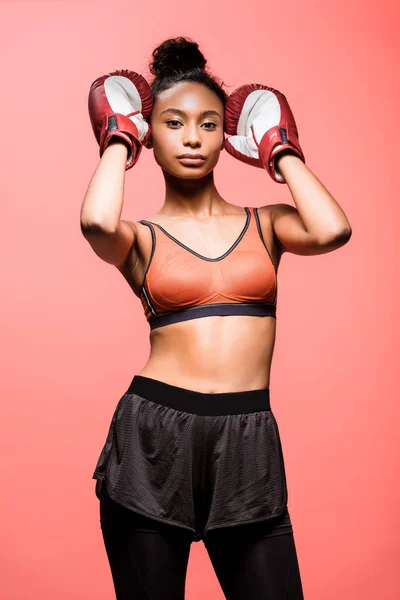 Attractive african american sportswoman in boxing gloves looking at camera isolated on coral — Stock Photo