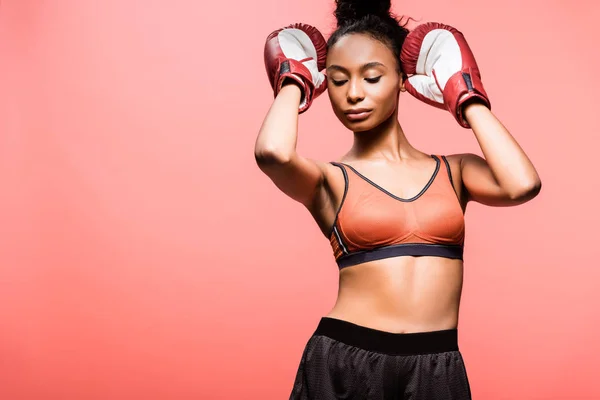 Beautiful african american sportswoman in boxing gloves posing isolated on coral with copy space — Stock Photo