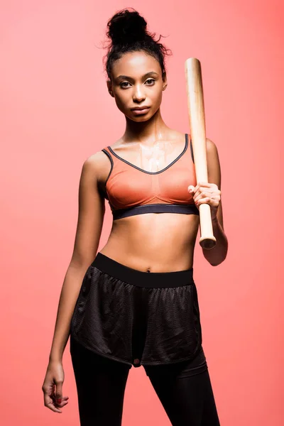 Schöne afrikanisch-amerikanische Sportlerin blickt in die Kamera und posiert mit Baseballschläger isoliert auf Korallen — Stockfoto