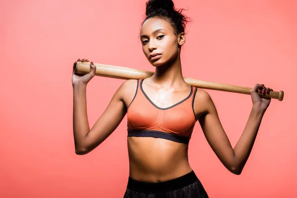 Beautiful african american sportswoman holding baseball bat and looking at camera isolated on coral — Stock Photo