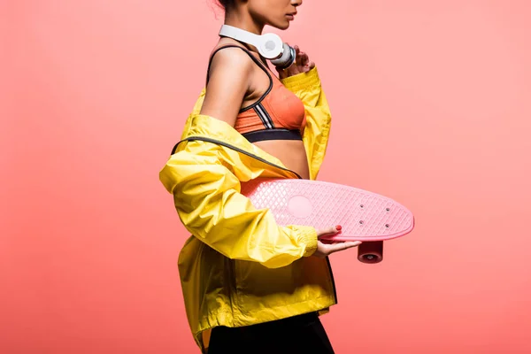 Cropped view of african american sportswoman with headphones holding penny board isolated on coral — Stock Photo