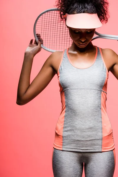 African american sportswoman in sun visor holding tennis racket isolated on coral — Stock Photo