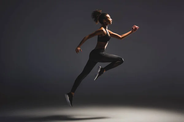 Vista lateral de hermosa atlética afroamericana deportista saltando en negro - foto de stock