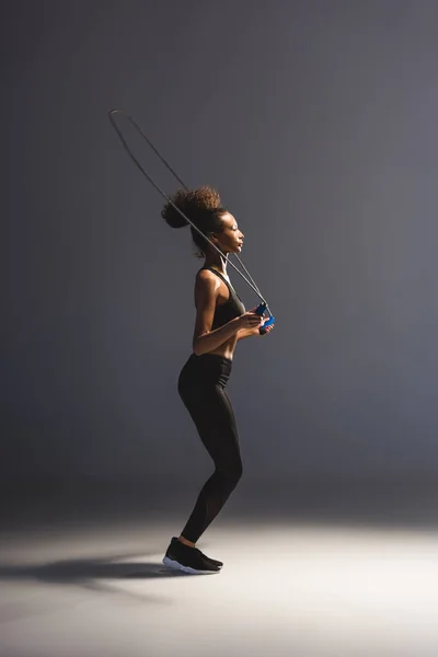 Atletica sportiva afroamericana che si allena con corda da salto sul grigio — Foto stock