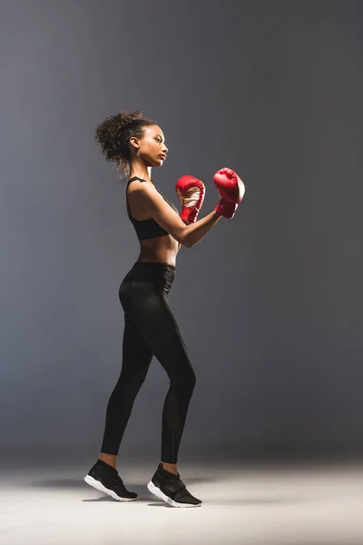 Beautiful athletic african american sportswoman in boxing gloves on black — Stock Photo