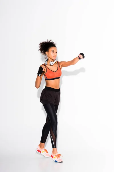 Hermosa atlética afroamericana deportista entrenamiento en guantes deportivos en blanco - foto de stock