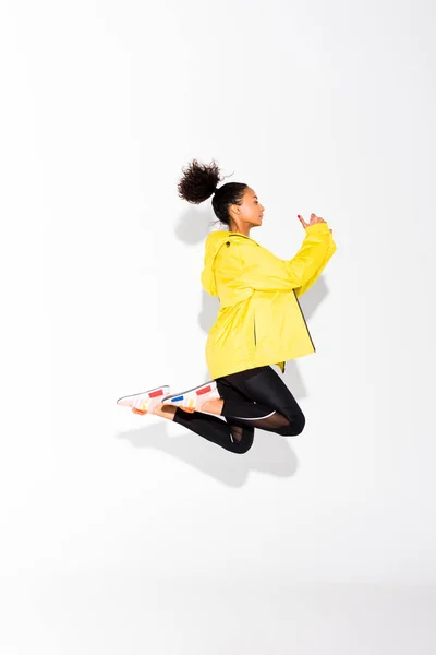 Vista lateral de la hermosa atlética afroamericana deportista saltando sobre blanco - foto de stock