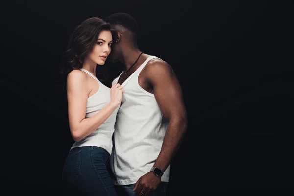 Hermosa pareja interracial seductora en camisetas blancas aisladas en negro con espacio de copia - foto de stock