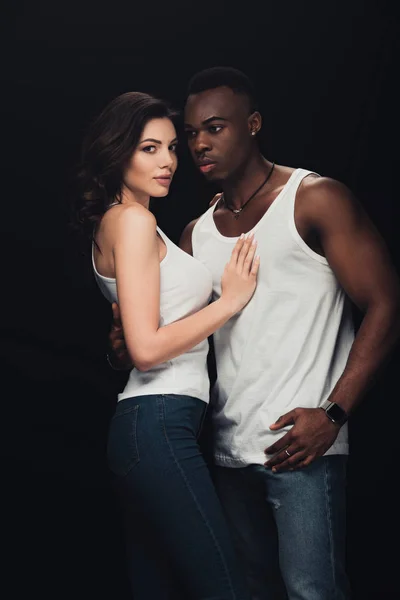 Hermosa pareja interracial seductora en camisetas blancas aisladas en negro - foto de stock