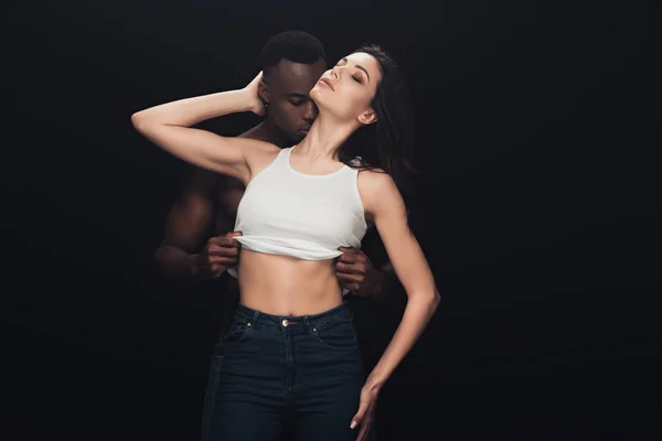 Handsome african american man undressing beautiful sensual woman isolated on black with copy space — Stock Photo