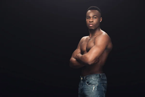 Sexy muscular africano americano hombre en denim con cruzados brazos mirando cámara aislada en negro - foto de stock