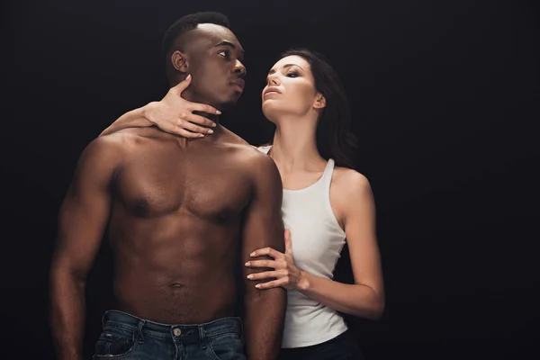 Bella donna seducente che abbraccia l'uomo afroamericano senza maglietta isolato sul nero — Foto stock