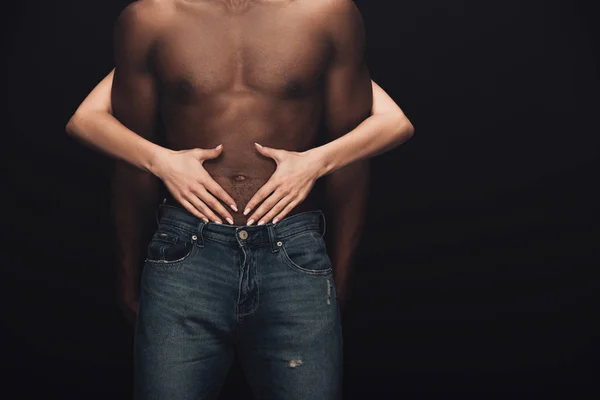 Vista ritagliata della donna che abbraccia uomo afroamericano senza camicia isolato su nero con spazio copia — Foto stock