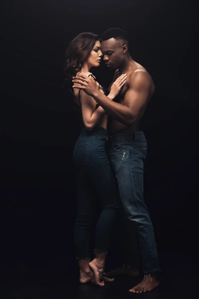 Beau couple interracial sexy en denim embrassant isolé sur noir — Photo de stock