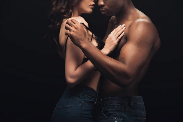 Recortado vista de sexy interracial pareja abrazando aislado en negro - foto de stock