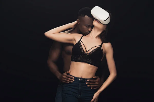 Afrikanische amerikanische Mann umarmt und küsst sexy Frau in Virtual-Reality-Headset isoliert auf schwarz — Stockfoto