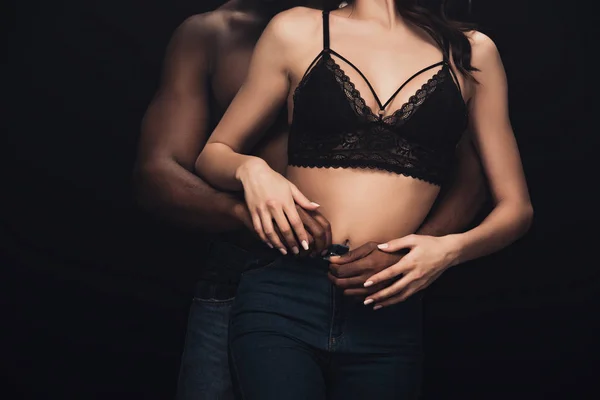 Corte vista de afro americano homem abraçando sexy mulher no lingerie isolado no preto — Fotografia de Stock